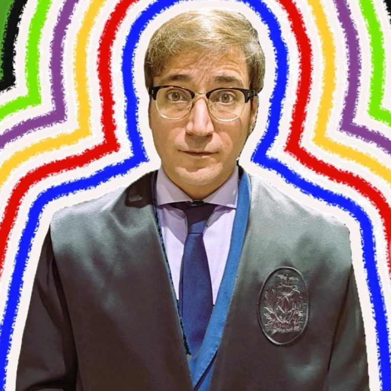 Hombre con gafas y traje oscuro, rodeado de un fondo multicolor en forma de arcos.